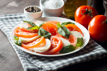 Photo of Caprese Salad with tomatoes, basil, mozzarella, olives and olive oil on wooden background. Italian traditional caprese salad ingredients. Mediterranean, organic and natural food concept.