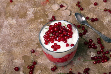 Healthy dessert with organic red currants, fresh yogurt and corn flakes. Dietary breakfast on a brown background