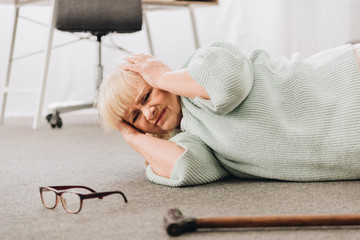 helpless retired woman lying on floor in living room while having headache