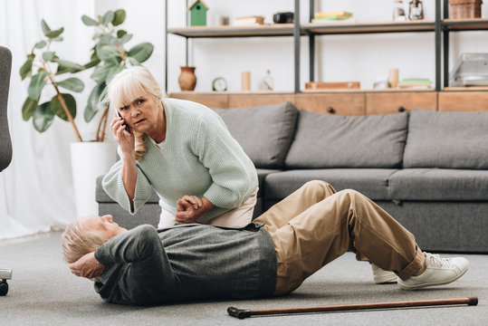 Senior Woman Holding Hand Of Dying Old Man With Walking Stick And Looking At Camera