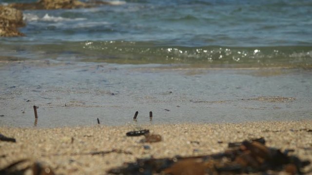 Breathtaking blue rippling water splash on the Cyprus sand beach in macro view with blur rocky background