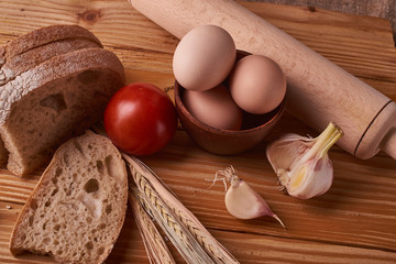 fresh delicious bread, concept for baking. Eggs in clay bowl, garlik, tomato and wheat sprouts on wooden table