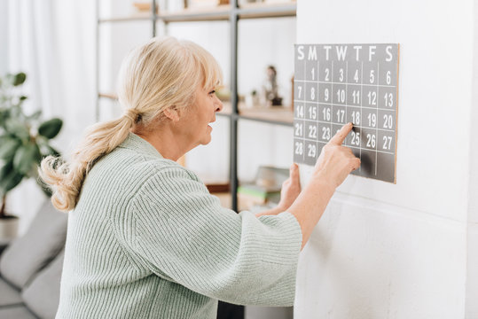 Senior Woman Touching Wall Calendar And Looking At Dates