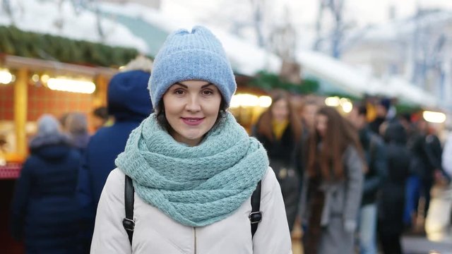 Portrait of a young woman smiling outdoors. She wears blue hat and scarf