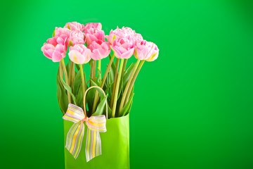 Flower bouquet of pink tulips in a vase with a multicolored bow tie on a bright green background, copy or text space