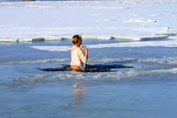 Fototapeta premium Winter sport. A woman swims in the winter river covered with ice during the holiday of Epiphany. Hardening
