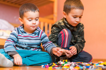 Two children playing with lots of colorful plastic blocks constructor sitting on a floor indoor. Two little brothers play constructor. Communication and friendship.