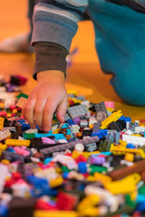 Close up of colorful plastic bricks on the floor. Early learning. Developing toys. Children's plastic constructor on the floor. Children's hands play a little constructor. vertical photo.