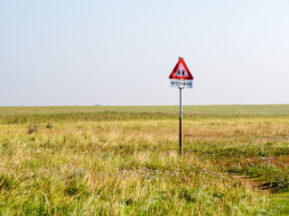 Quicksand danger warning sign in coastal saltmarsh of West Frisian island Schiermonnikoog at low tide of Waddensea, Netherlands
