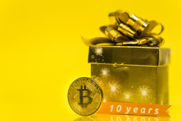 Bitcoin celebrating birthday, coin with birthday golden present behind it and 10 years sign, with yellow copy space