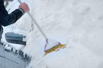 Driver cleans with broom the pure white snow over the car on the parking outdoor. Weather forecast,...