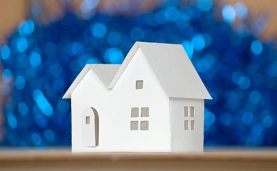 Handmade small white cardboard houses with cut windows on dark blue bokeh background. Winter...