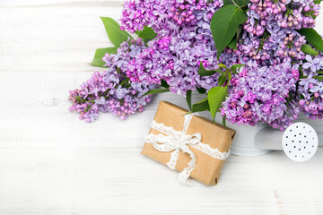 Lilac flowers and gift box on white wooden background, copy space