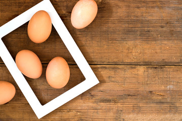 Frame with eggs inside on brown wooden background texture