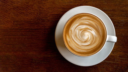 Hot coffee cappuccino latte spiral foam top view on wooden background