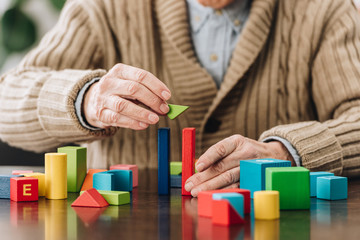 cropped view of retired man playing with wooden toys on table - obrazy, fototapety, plakaty