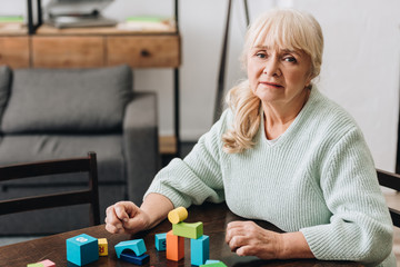 retired woman with blonde hair sitting near wooden toys at home