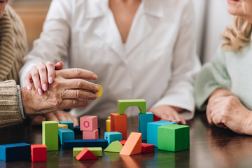 cropped view of senior couple and caregiver playing with wooden toys