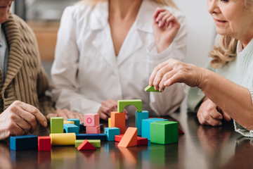 cropped view of woman sitting with retired couple and playing with wooden toys