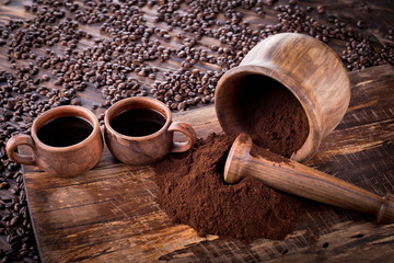 Two mugs of clay with coffee stand on a wooden board. Against the background of a mortar with...