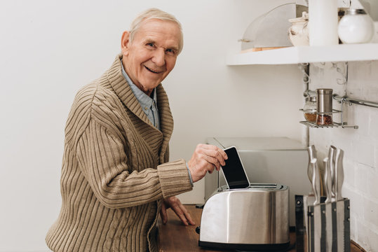 happy senior man with dementia disease putting smartphone in toaster
