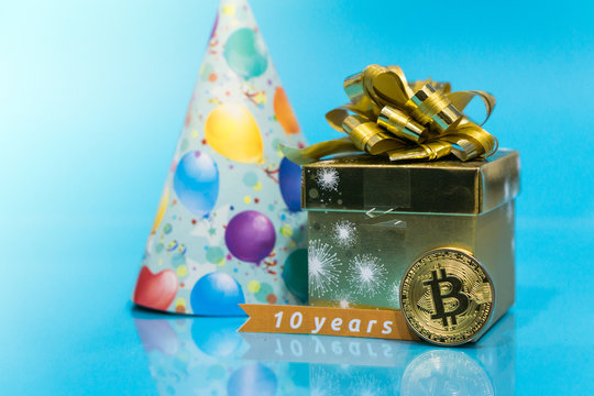Bitcoin 10 year anniversary, coin with birthday golden present and birthday hat behind it and 10 years sign, copy space