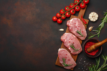 Pieces of raw pork steak with basil, cherry tomatoes, rosemary, garlic, pepper, salt and spice...