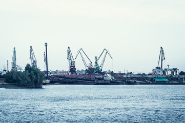 A barge in the river port and working cranes on the city background 