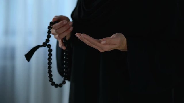 Arab female in hijab counting prayers by rosary in hand, religious forgiveness