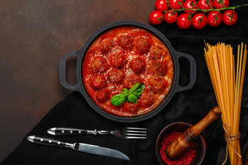 Meatballs in tomato sauce with spices, cherry tomatoes, pasta and basil in a frying pan on rusty brown background