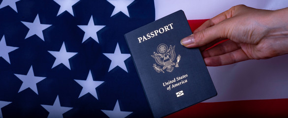 Female hand holding Passport of USA on American glag background. Wide photo.