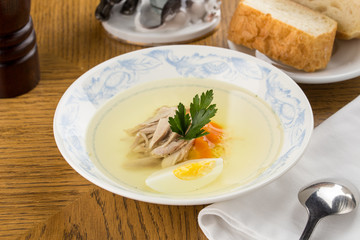 Low fat chicken broth with a half cooked egg and parsley in a glass bowl on wooden table