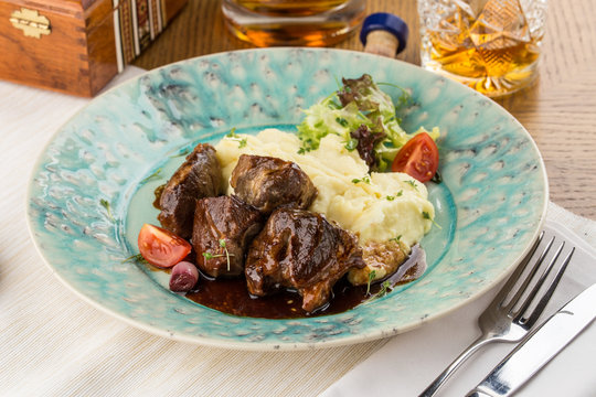 Beef stew with mashed potatoes and fresh vegetables on wooden table