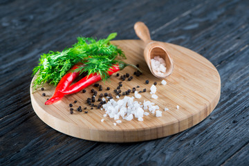 rock salt lies on a wooden surface against the background of grains of black pepper, red pepper and dill