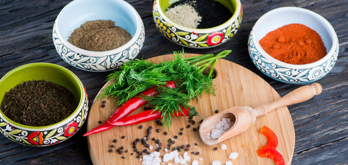 rock salt lies on a wooden surface against the background of grains of black pepper, red pepper and dill. There are various seasonings in the containers.