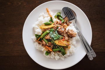 Rice topped with stir fried beef and basil. Put the dish white. on the table Brown