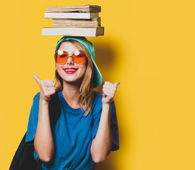 Young style student girl with orange glasses and books on yellow background. Clothes in 1980s style