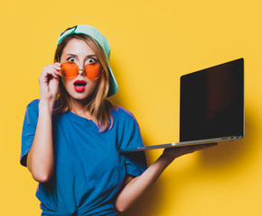 Young style girl with orange glasses and laptop computer on yellow background. Clothes in 1980s...