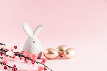 Naklejka na ściany i meble Easter golden eggs, pink flowers and porcelain rabbit on pastel pink background. Easter, spring concept. Copy space, banner