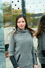 Close-up outdoors portrait of a beautiful smiling fashion looking girl with long hair in gray coat.