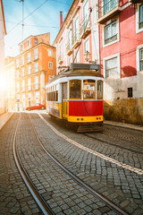 Fototapeta na wymiar Touristic vintage red tram in a Lisbon street on sunny afternoon, narrow streets, cobblestones winding road, vacation in Lisbon.