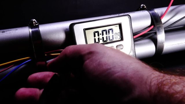 Hand cuts wire to defuse pipe bomb with clock timer counting down, handheld motion