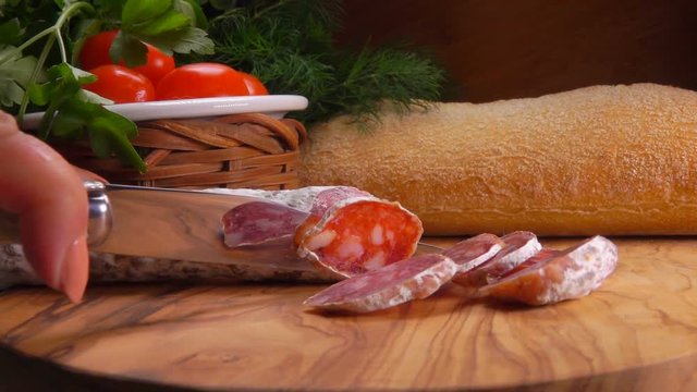 Chef cuts off a piece of smoked spicy sausage on a wooden board very close-up
