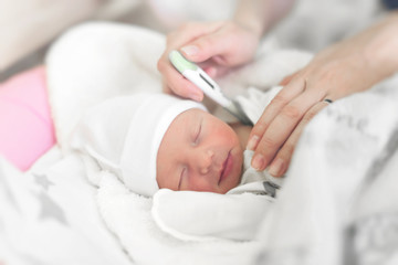 Baby girl in the crib measures body temperature. Mom measures the baby's body temperature with a...