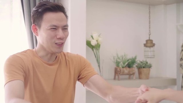Slow motion - Asian couple dance while listen to music in living room at home, sweet couple enjoy love moment while lying on the sofa when relax at home. Lifestyle couple relax at home concept.