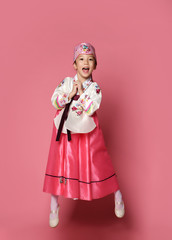 Korean little baby girl in traditional silk dress for new year celebration dancing jumping on pink with hands spread