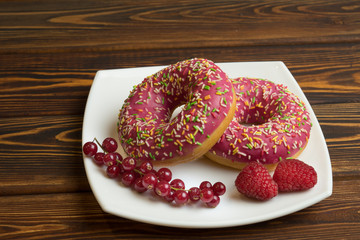 Donuts with icing and berries, on the plate, on dark wooden background