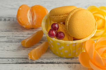 Colorful macaroons on the white wooden table. Sweet macarons with tangerines and currant . Top view