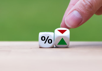 Hand is turning a dice and changes the direction of an arrow symbolizing that the interest rates...