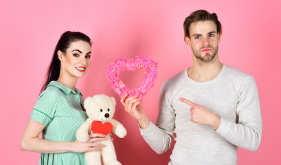 Fototapeta na wymiar Handsome man and pretty girl in love. Romantic couple in love. Cute gift concept. Valentines day and love. Man and woman couple in love hold heart valentines cards and teddy bear on pink background